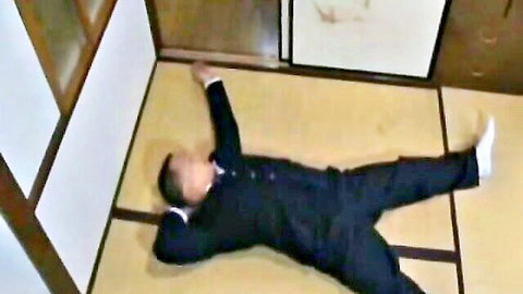 Asian man in dark suit lying spread-eagled on tatami floor