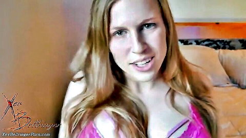Blonde woman in pink lingerie teasing with open mouth on bed