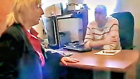 British mature blonde woman in office attire interviewing older man at desk