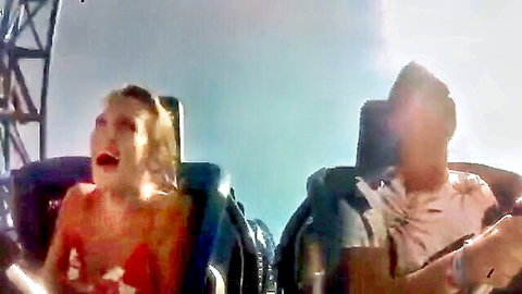 Blonde in red dress screams excitedly on rollercoaster ride with man beside her