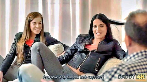Two young brunettes in leather jackets chat intimately with older man on couch