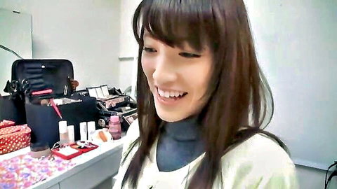 Smiling Asian woman with long dark hair in white cardigan at vanity