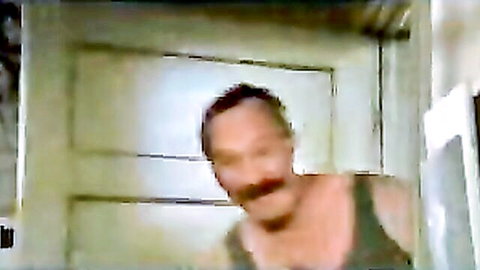 Blurry mustachioed man in tank top standing by white door in low-res clip