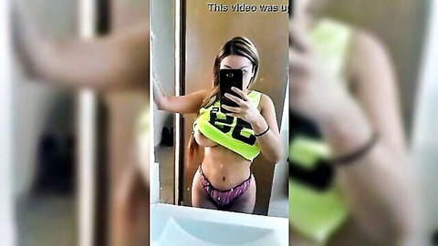 Petite blonde with big tits in low-cut green tank top and purple thong panties poses in bathroom mirror selfie