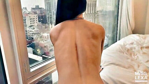 Nude brunette with big juicy ass stands by window exposing bare back and city skyline