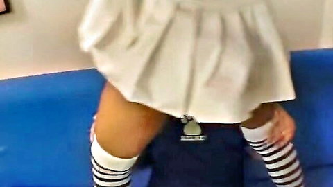 Shemale in white pleated skirt and striped stockings bent over couch