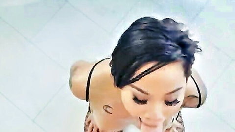 Tattooed Asian babe with big tits sucks white lollipop teasing blowjob on tiled floor
