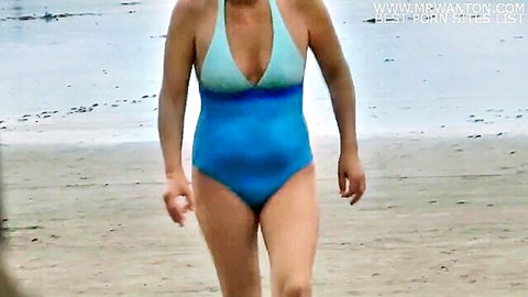 Mature blonde wife in teal swimsuit teasing on sunny beach