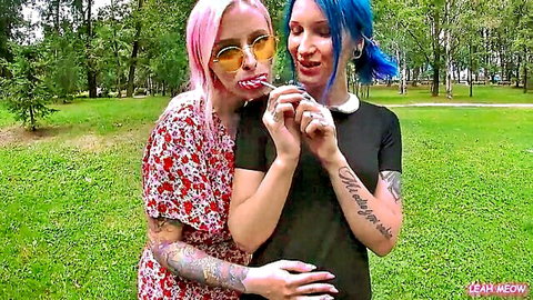 Tattooed pink and blue haired babes teasing with lollipop suck in public park