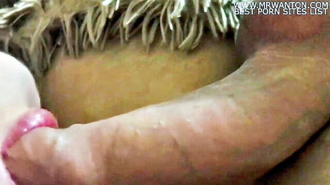 Close-up of erect cock held by hand with pink nails near woman's lips for blowjob tease