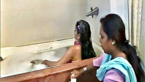 Two Indian women in bathtub, one nude washing long wet hair, other helping in saree
