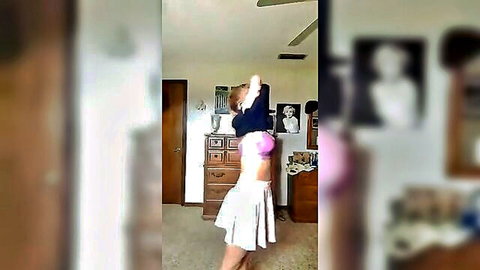 Brunette undressing in bedroom, lifting top to show pink bra and skirt
