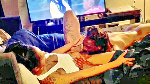 Ebony couple in intimate couch embrace, tattoos visible