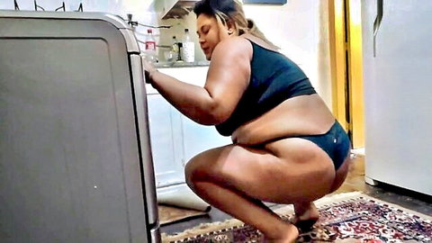Curvy black stepmom in black bra and thong squatting teasingly in kitchen