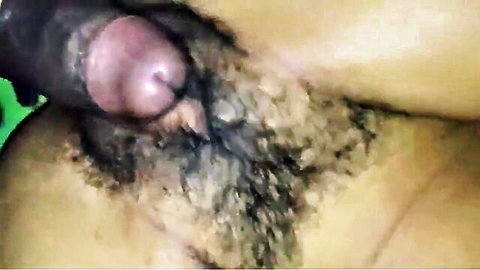 Closeup of erect black cock head glistening with precum surrounded by bushy pubes