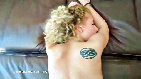 Skinny blonde teen with small ass and green back tattoo lying nude face down on leather couch