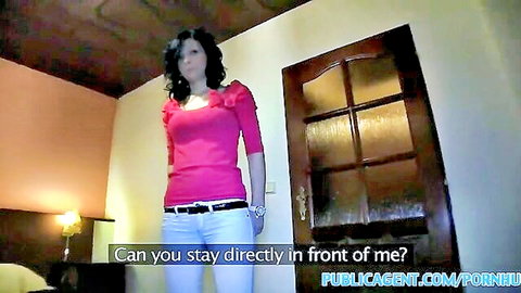 Brunette in pink ruffled blouse and white jeans standing in hotel room