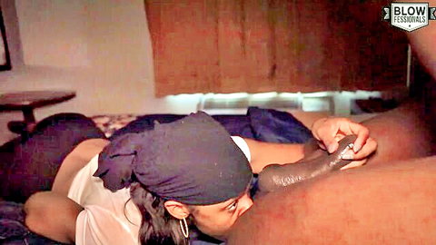 Ebony MILF in purple headwrap grips massive black cock with her hand to her lips for blowjob
