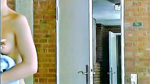 Topless blonde with perky tits holding blue towel over pussy in brick bathroom