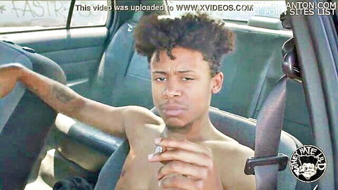 Lil D shirtless in car, afro hairstyle, intense gaze while smoking