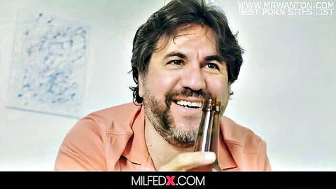 Smiling bearded man in orange shirt holds beer promoting MILF porn sites like MILFEDX