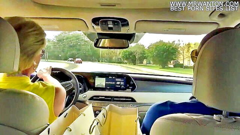 Blonde mature woman in yellow top driving car with male passenger, teasing vibe