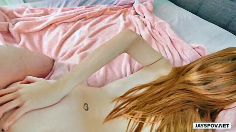 Redhead with heart tattoo lying nude on bed reaching hand out in POV