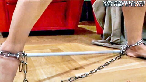 Woman's slim legs and bare feet locked in metal shackles with spreader bar