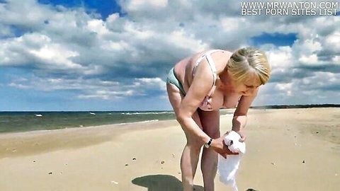 Blonde mature wife in bikini bending over on sunny beach