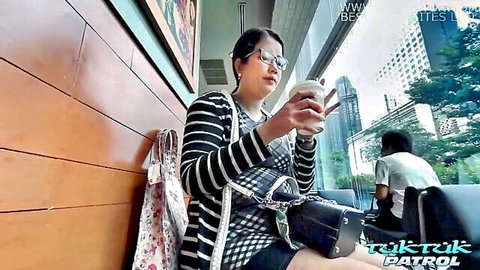 Plump Asian woman with big booty in striped cardigan and glasses at cafe