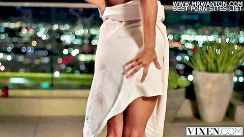 Brunette college student in teasing white wrap on city balcony at night