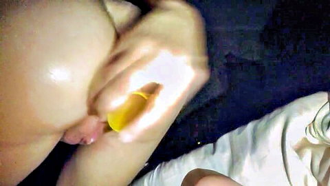 Pale-skinned woman holding yellow condom near exposed intimate area in dim light