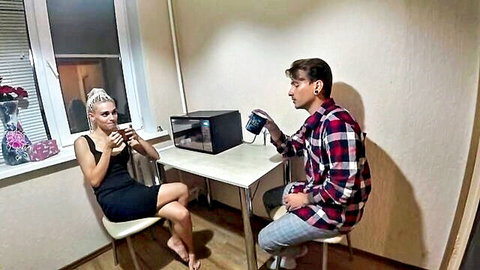 Blonde woman in short black dress sits with man holding device in intimate chat