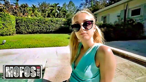 Anastasia Knight, blonde in pigtails and sunglasses, sitting poolside in low-cut teal top