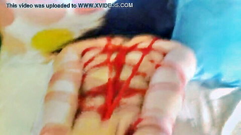 Homemade bondage scene with nude woman tied in red ropes on bed