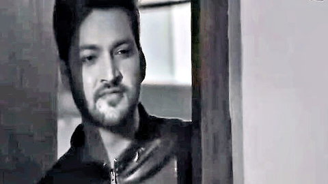 Handsome bearded South Asian man in leather jacket leaning intensely against wooden door frame