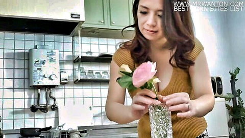 Mako Oda holding pink rose in vase, deep cleavage in low-cut top