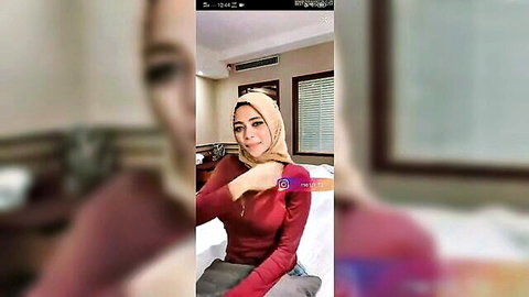 Sexy Malaysian hijab woman smiling seductively in tight maroon top on bed