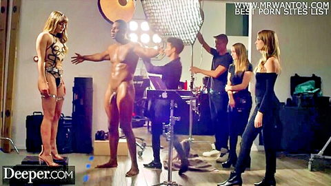 Naked muscular black stud with massive erect BBC posing on porn set surrounded by hot blondes