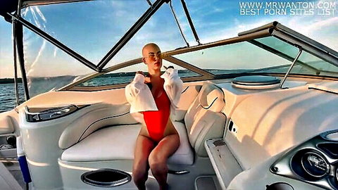 Bald woman in red swimsuit and open white shirt poses seductively on boat