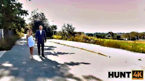 Eveline Dellai in sexy white dress walks with suited man in Hunt4K outdoor scene