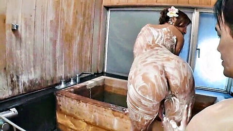 Soapy naked Japanese woman bent over wooden bathtub showing bubbly ass to aroused man in steamy onsen