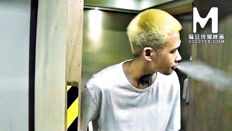 Tattooed Asian man with blonde hair exhaling smoke in white t-shirt