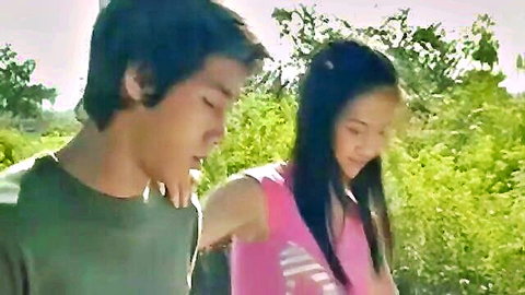 Young Asian couple walking intimately in lush green outdoor field