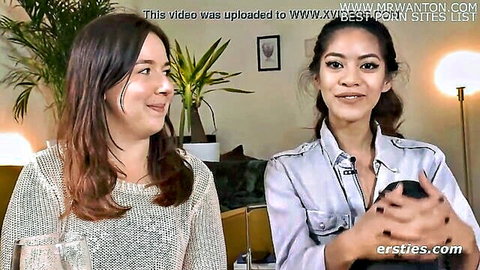 Two smiling clothed lesbians on couch teasing with big natural tits in cozy room