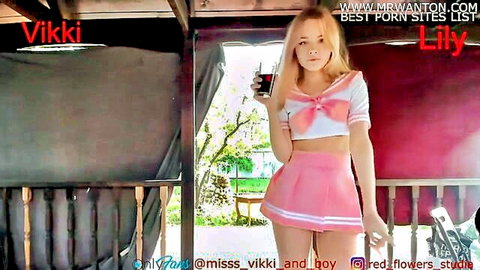 Blonde teen in tiny pink sailor skirt and cropped top posing sexy with drink on balcony