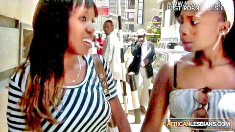 Two sexy ebony lesbians flirting closely on busy street in tight tank tops