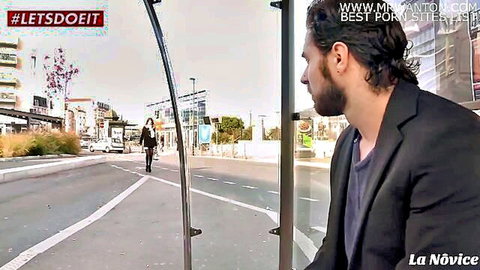 Curly-haired man in suit stands at outdoor bus stop on urban street ready for pickup seduction.