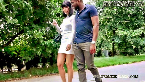 Sexy long-haired brunette in tight white mini dress walks arm-in-arm with muscular black stud in sunny park