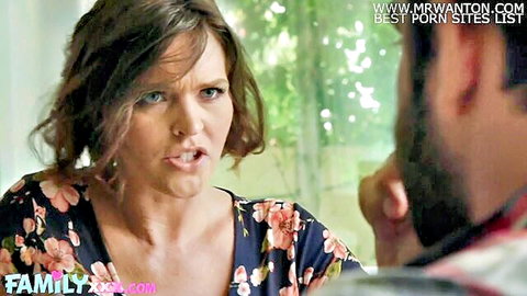Shocked brunette MILF in floral dress leans forward with intense expression facing man's gesturing hand